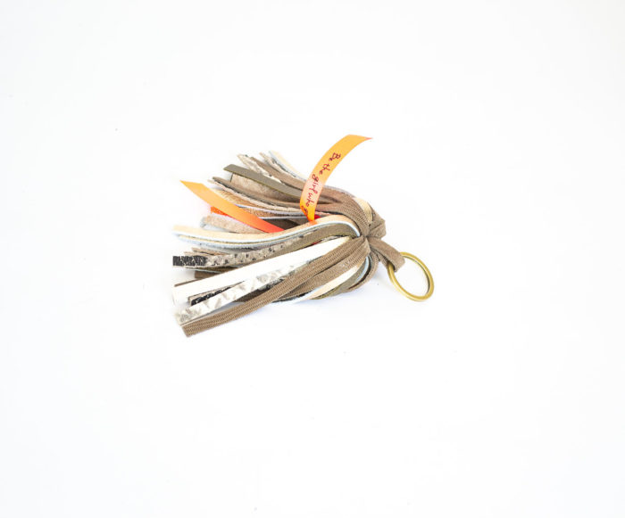 Close-up of the product: a keyring with beige and light gold leather fringes.